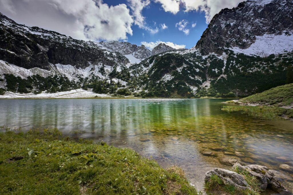 Captivating alpine lake view surrounded by snow-dusted mountain peaks under a vibrant sky.